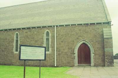 A grey stone church with an Irish-language notice board — Dingle Peninsula, Ireland (4-9 July 2000)