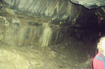 A woman in a red jacket exploring a dim cave passage — Ireland, Ireland (4-9 July 2000)