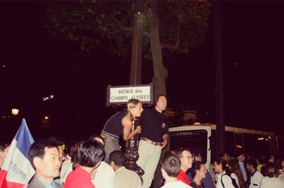 Revellers climbing a Champs-Elysees street-name lamppost — Paris, France (2-8 July 2000)