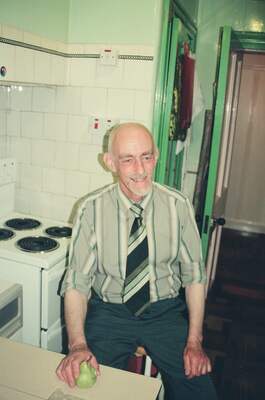 A smiling bald man holding a pear in a tiled kitchen — Edinburgh, Scotland (August 2000)