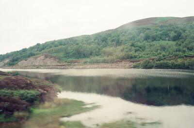 Wooded slopes reflected in a quiet Highland loch — Scottish Highlands, Scotland (late July 2000)