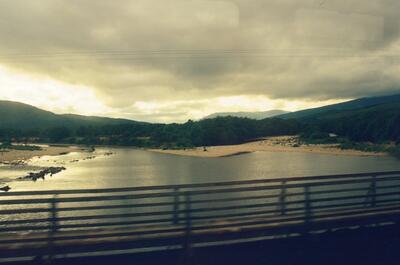 A wide gravel-banked river curving below cloudy hills — Fort William, Scotland (August 2000)