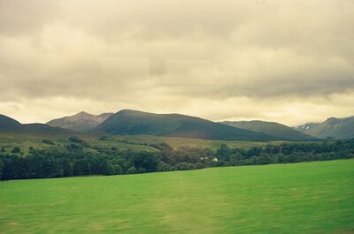 A sweep of green fields below craggy mountain peaks — Scottish Highlands, Scotland (August 2000)