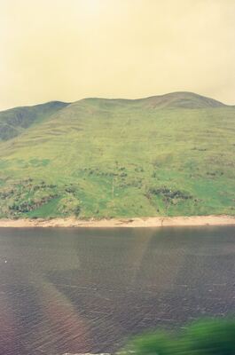 A pale beach edging a loch below green hills — Scottish Highlands, Scotland (August 2000)