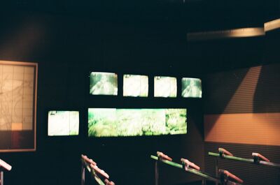 A bank of glowing video screens above wooden rails — London, England (August 2000)