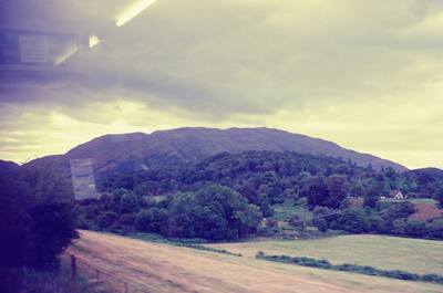 A wooded hill and farmland seen from the train window — Scottish Highlands, Scotland (late July 2000)