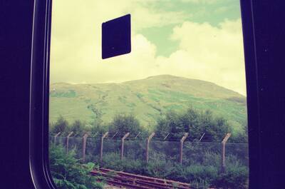 The train window framing a green hillside and railway — Scottish Highlands, Scotland (late July 2000)